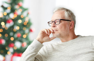 Senior gentleman contemplating next to a Christmas tree.