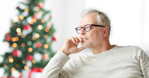 Senior gentleman contemplating next to a Christmas tree.
