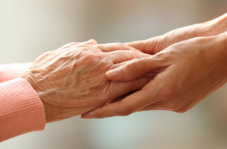 elderly woman's hands being held by a hospice volunteer.