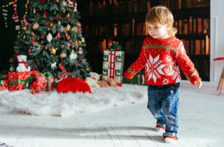 Toddler in sweater by a Christmas tree.