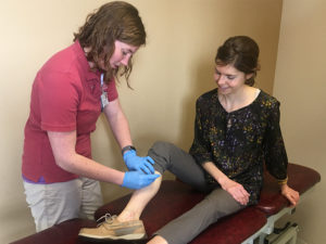 Female physical therapist performing dry needle therapy on a female patient in office.