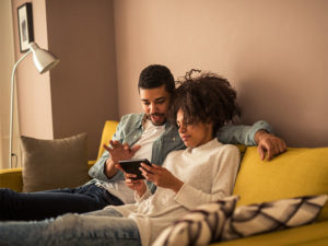 African-American couple on a couch surfing the web on a tablet.