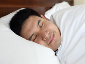 Asian-American man sleeping in a bed. 