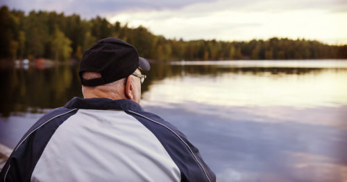 senior man contemplating while staring at a lake outside