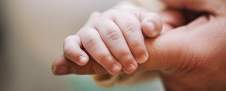 Infant hand wrapped around a finger of a congential heart specialist
