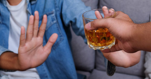 person saying no to friend offering glass of whiskey