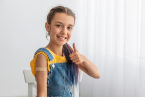 Young girl gives a thumbs up with a bandage on her arm after receiving a vaccine.