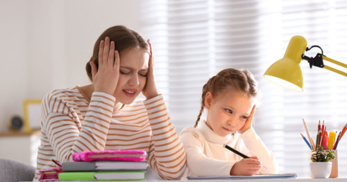 Stressed mother helping daughter with homework.