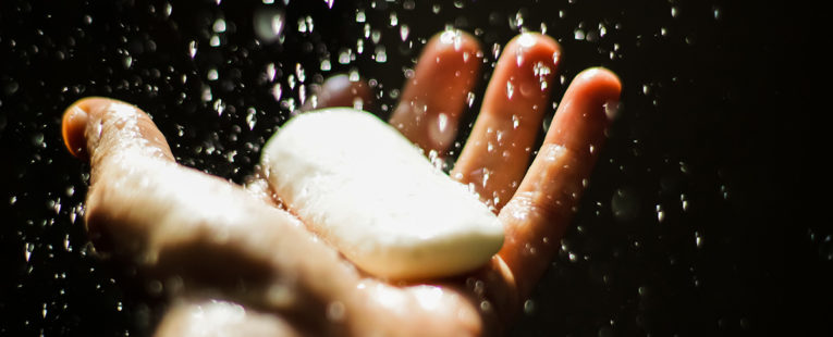 Man's hands holding a bar of soap getting wet.