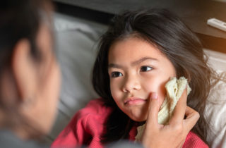 Mother wiping young daughter's cheek with cool washcloth to determine what the sick person needs.