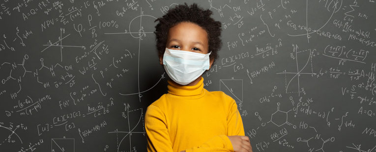Young African-American child in yellow shirt standing in front of chalkboard with chemistry formulas.