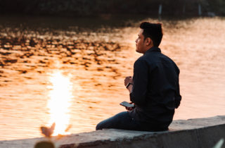 Young man sitting by a river staring off into the distance