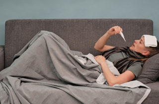 Woman with fever taking temperature on couch.