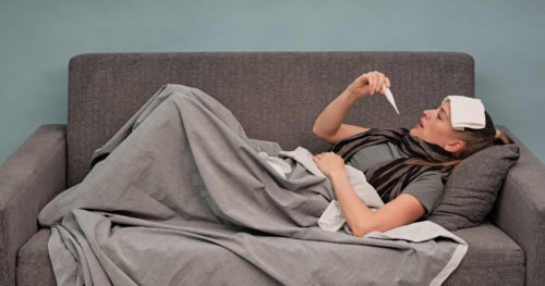 Woman with fever taking temperature on couch.