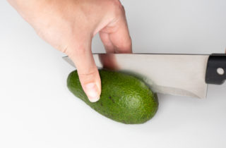 hand with knife using the proper method to safetly cut into an avocado