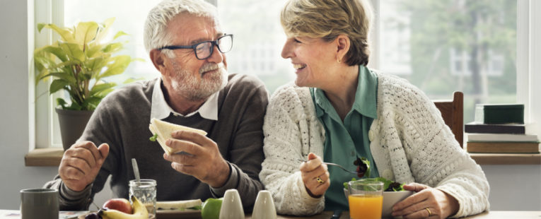 male and female seniors eating healthy food smiling at each other