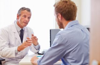 male physician sitting down and conversing with a male patient