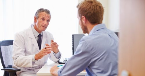 male physician sitting down and conversing with a male patient