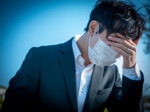 masked businessman holds his head shielding his eyes on a blue background