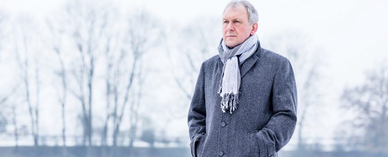 senior man stands solemnly outside in a coat and scarf during winter