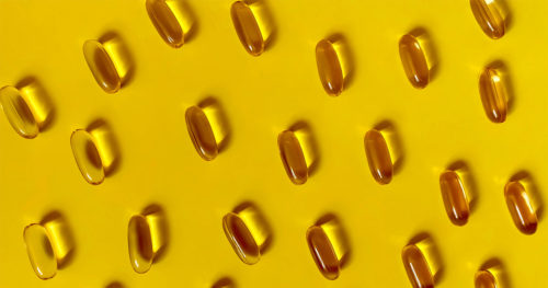 Vitamin D capsules on yellow background.
