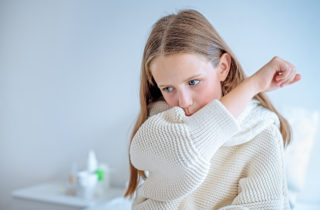 Girl in white sweater coughs into elbow