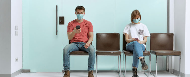 man and a woman sit wearing masks in a waiting room