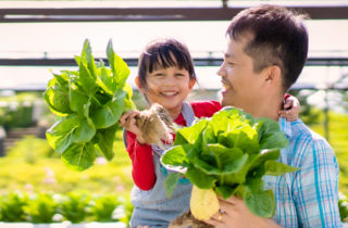 father holds his daughter and both are holding freshly picked vegetables
