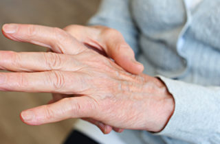 Person holding one hand in the other as though experiencing arthritis pain
