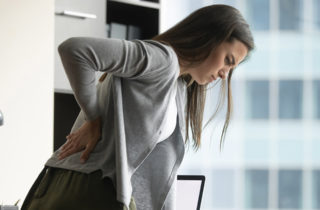 Woman standing at desk holding lower back as if in pain