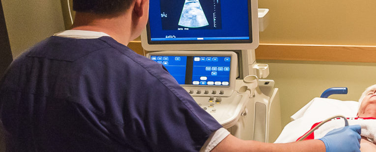 Technician performing ultrasound on senior woman patient with abdominal aortic aneurysm.