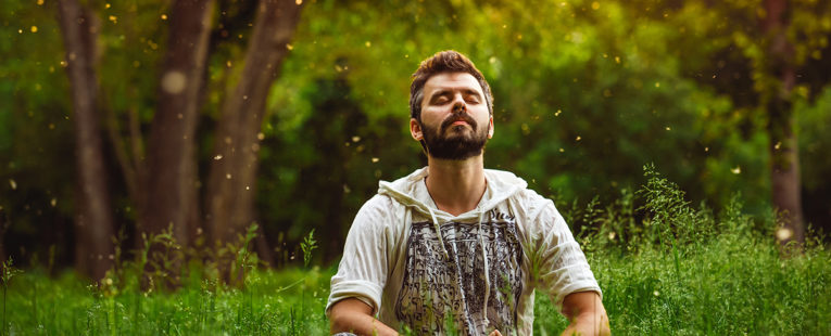 Man practicing progressive muscle relaxation sitting in a field with eyes closed