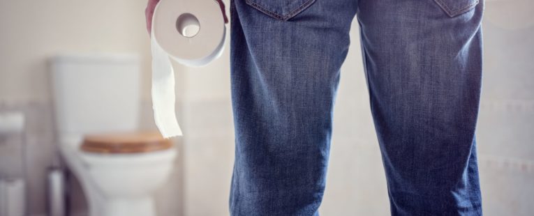 Man standing in bathroom with toilet paper