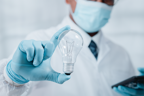 Doctor in surgical mask holds light bulb in foreground with blue gloved hand