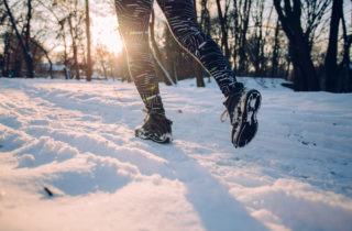 Sun shines in the background of a wooded area as a runner runs through the snow in the foreground