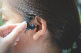 A close up woman with dark hair putting an earbud into her ear.