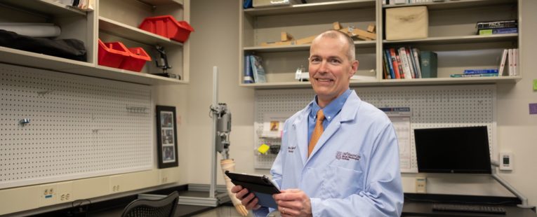 Christopher Zallek, MD, stands in the NeuroHealth Lab with a clipboard