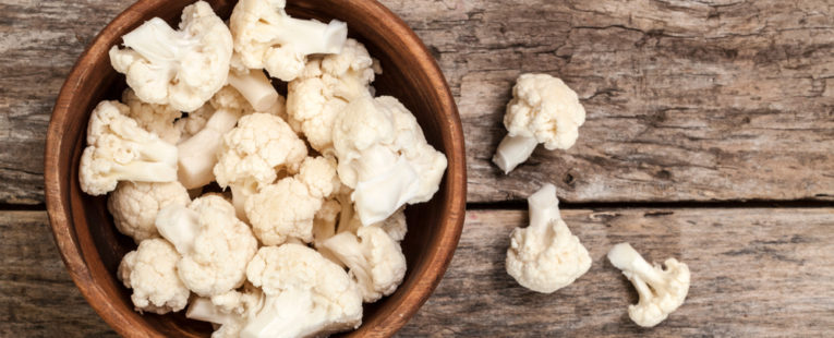 Pieces of cauliflower sitting in a wooden bowl. Cauliflower can be a healthy substitute for meal-time favorites.