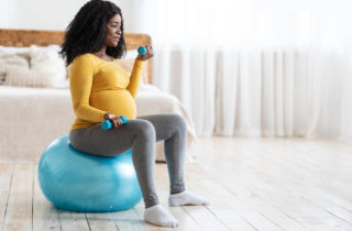 A pregnant woman sits on an exercise ball and holds weights to safely work out during pregnancy.