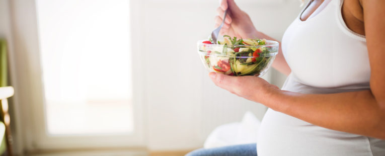 A pregnant woman eats a salad while learning about what to eat during pregnancy.