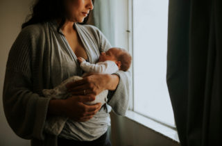 A woman holds her baby, who is not smiling, possibly due to postpartum symptoms.