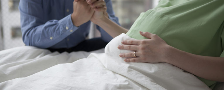 woman in hospital bed with husband, possible preterm labor, holding hands