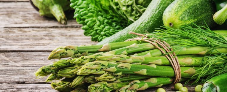 savor the season, spring into fresh produce, asparagus and green, leafy vegetables on a wooden table.