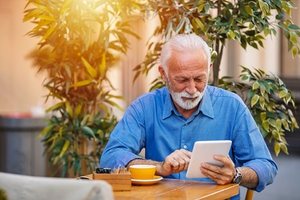 Senior man looks at a tablet while at a table with a cup of coffee